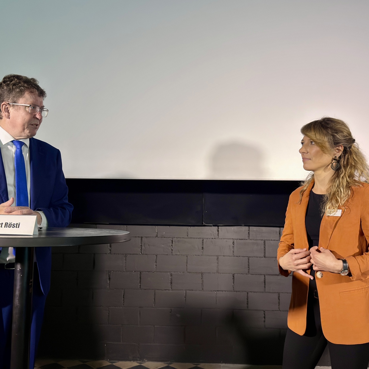 Bundesrat Rösti und Greta Gysin stehen sich gegenüber und diskutieren über die kritischen Fragen